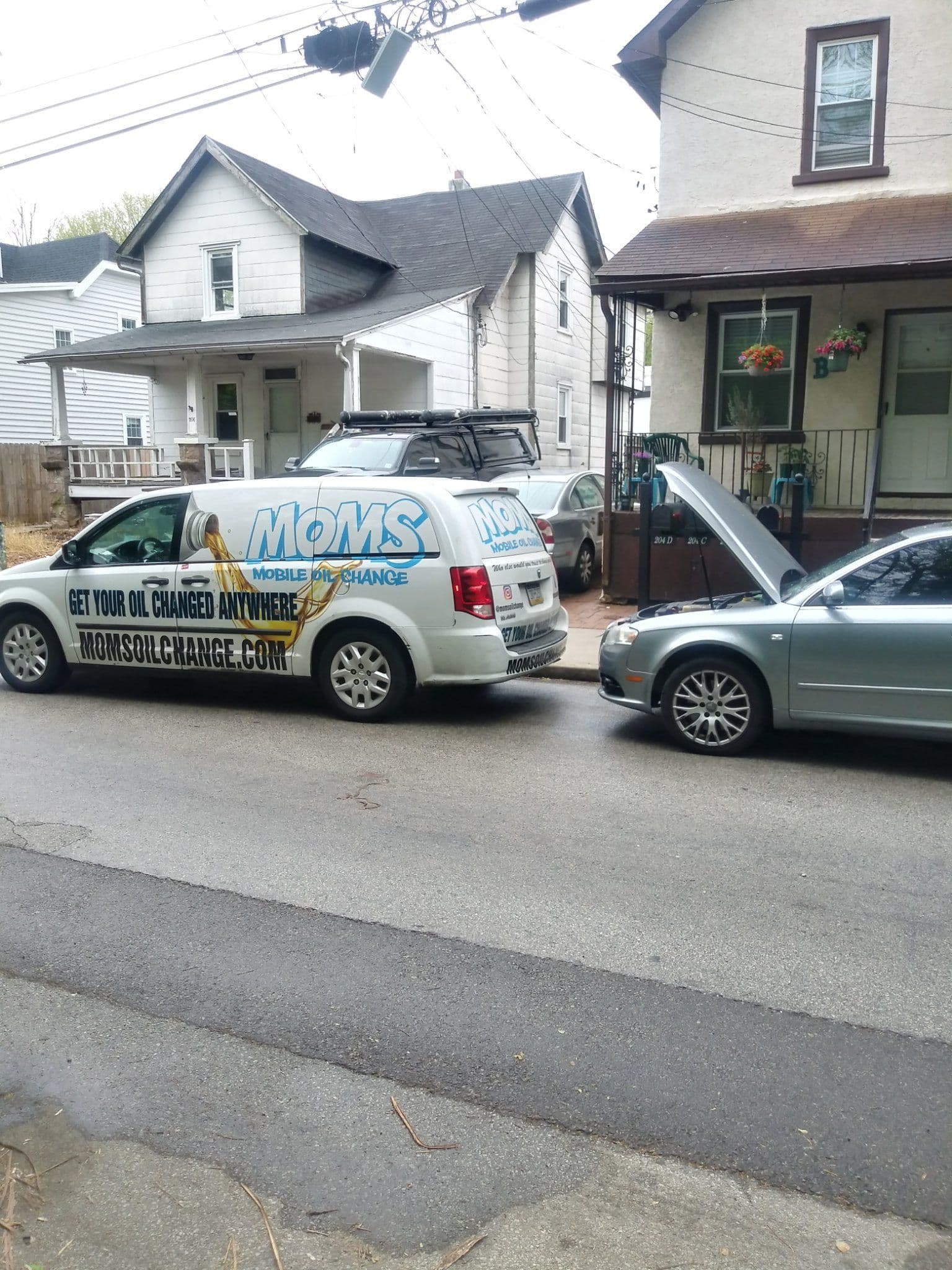 The MOMS van parked beside a customer's car with its hood up during a mobile oil change