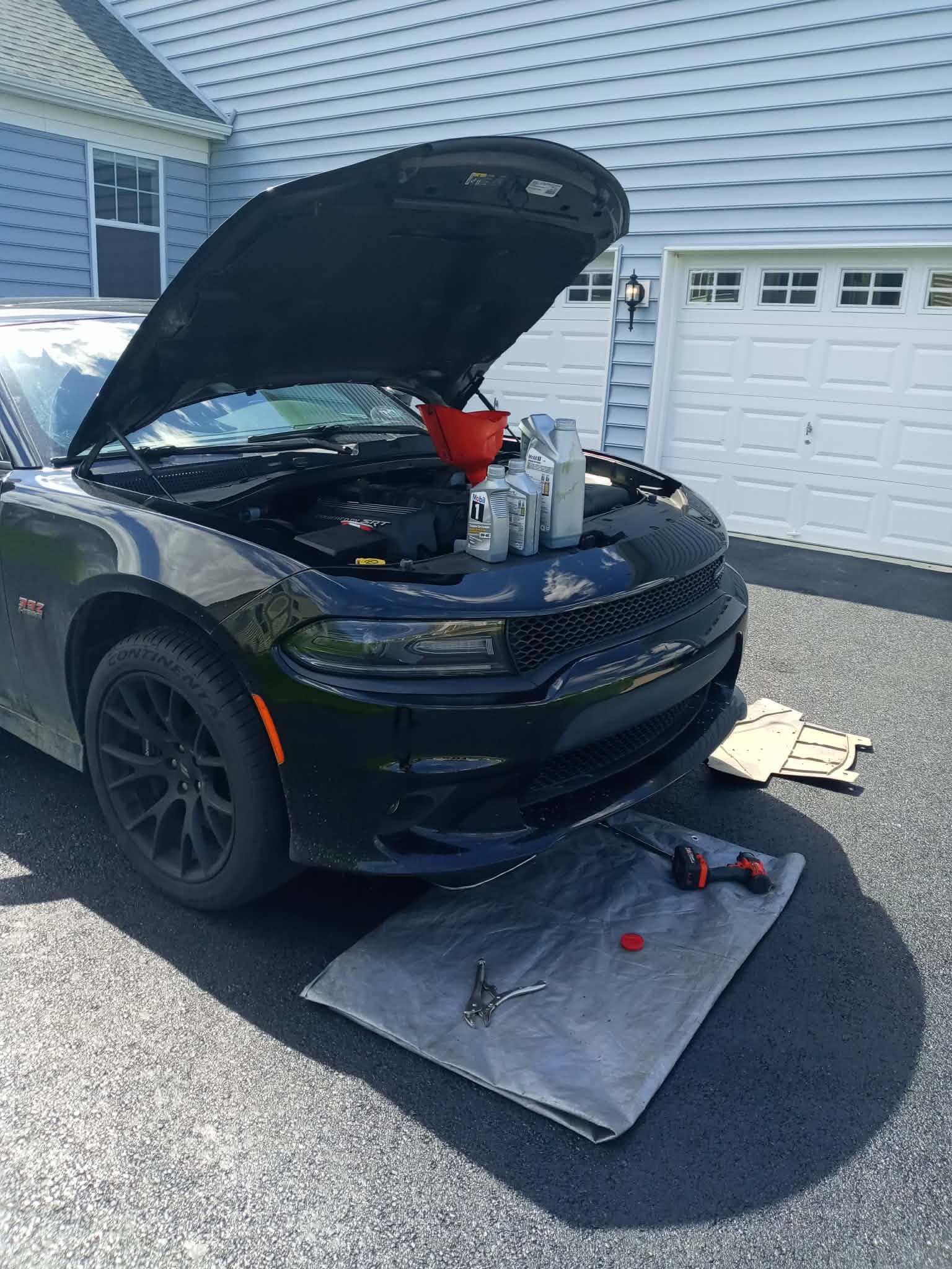 Mobil 1 full synthetic oil being poured into the engine of a black sports sedan during a mobile oil change