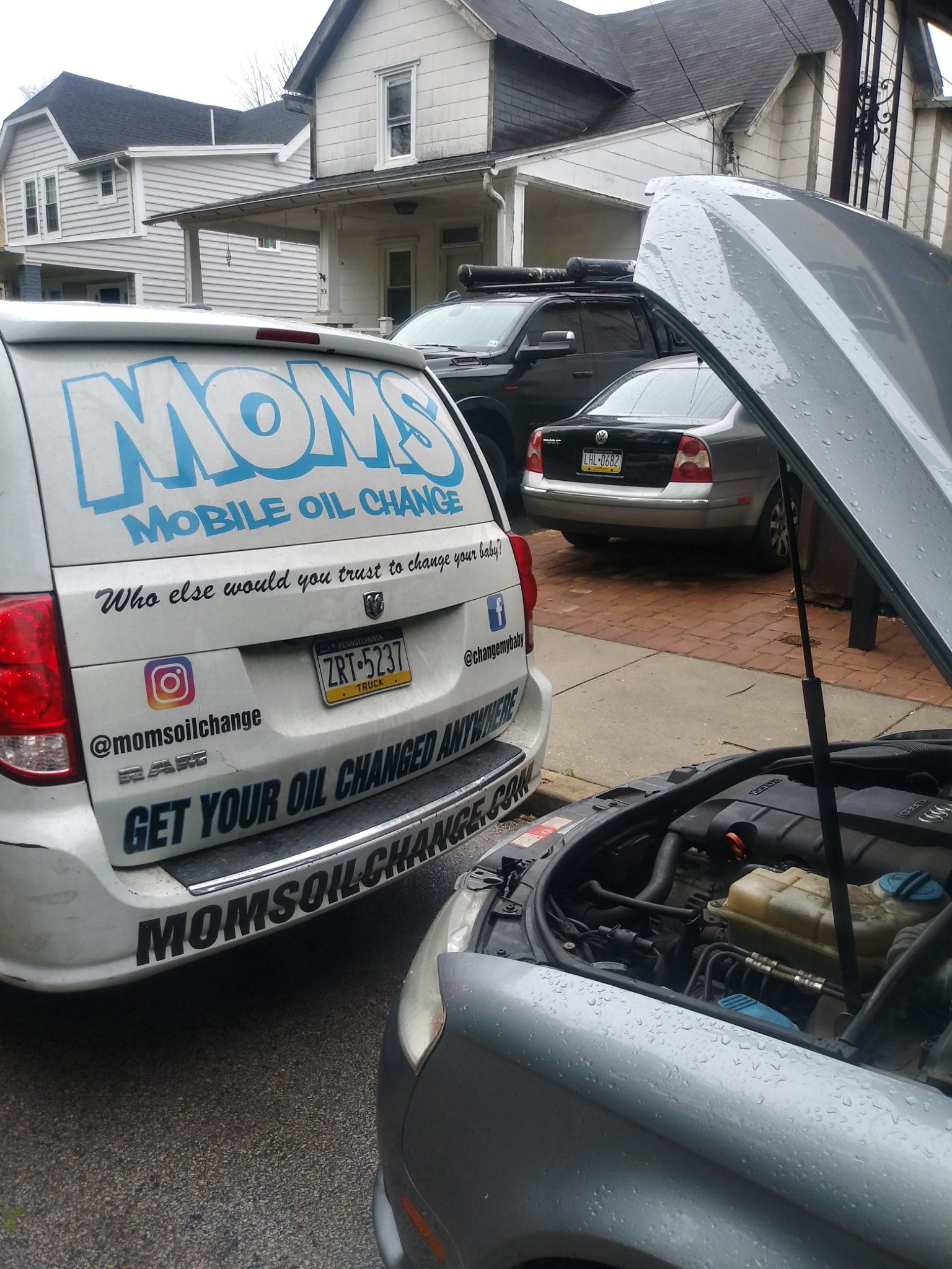 The MOMS van parked behind a customer's car during a driveway oil change.