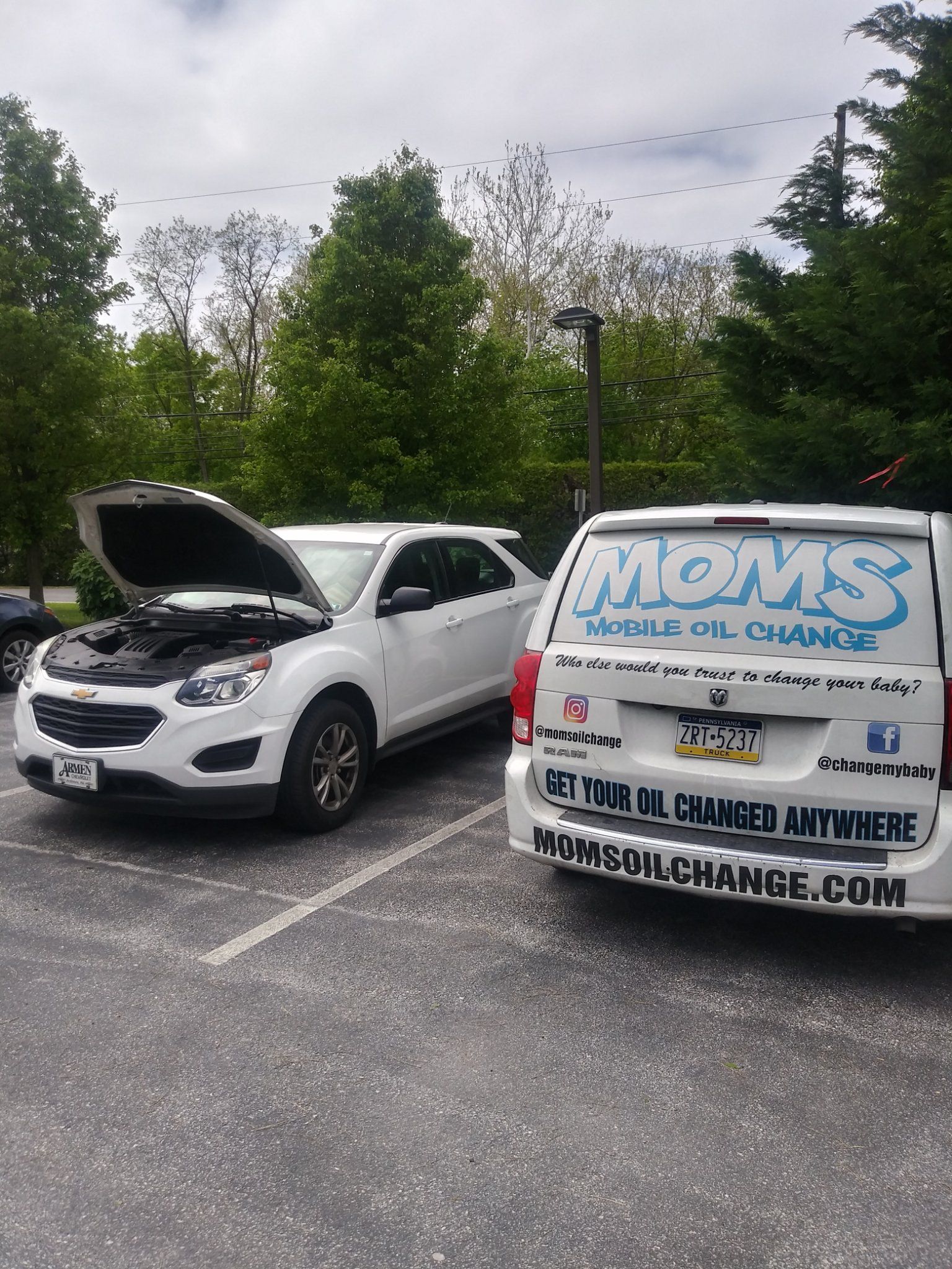 The MOMS van behind a white SUV with its hood up during a mobile service visit.